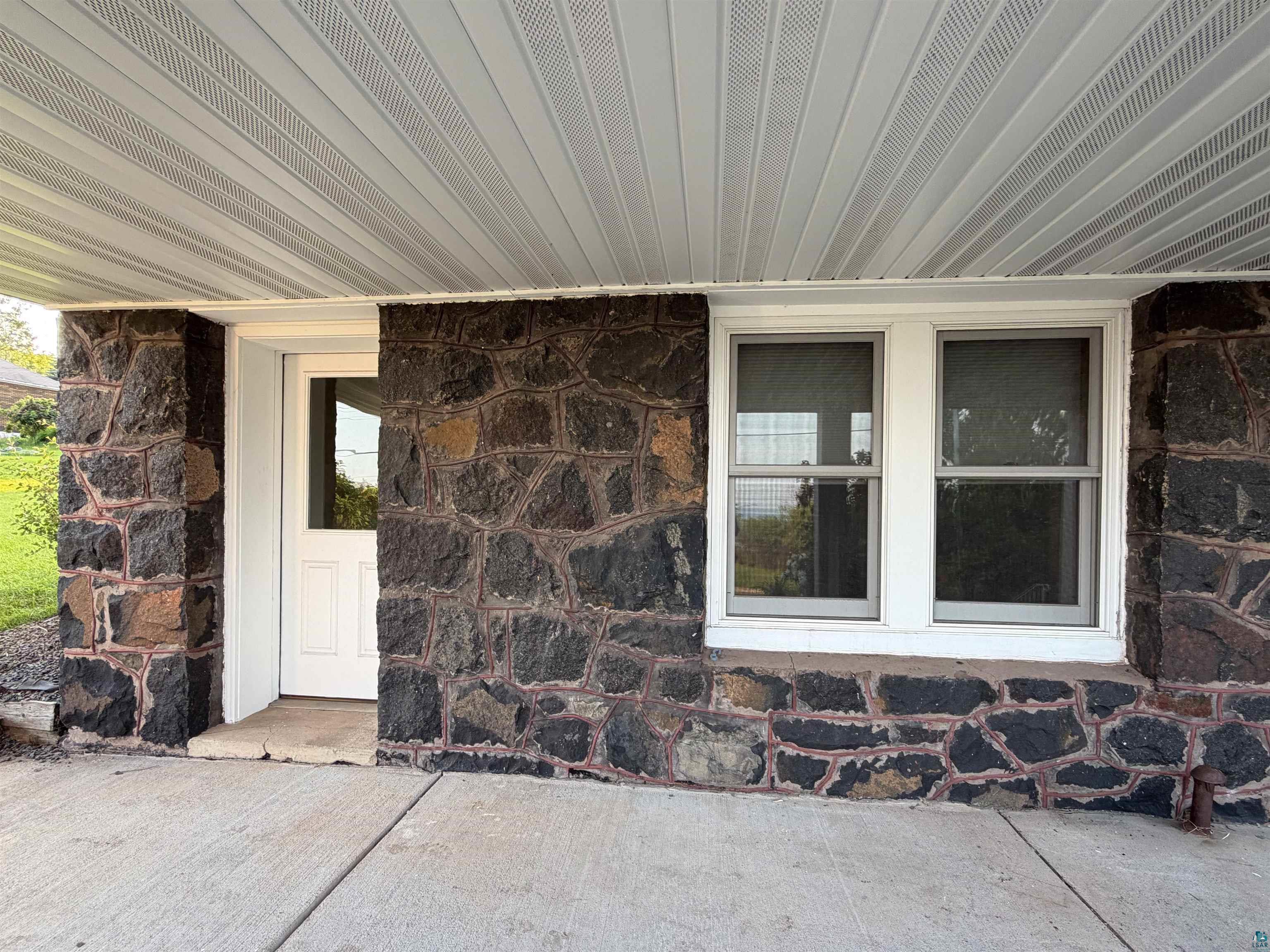 13 West 8th Street Duluth, MN 55806 - Photo 54 of 57 Stone facade exterior featuring a white paneled door, twin windows, a concrete patio, and a vented soffit ceiling