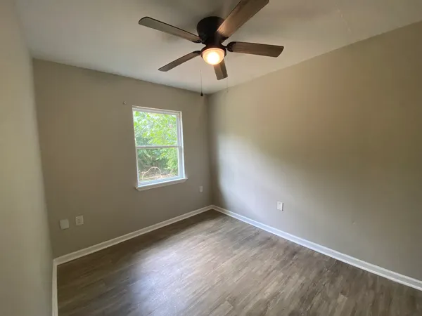 an empty room with wooden floor fan and windows
