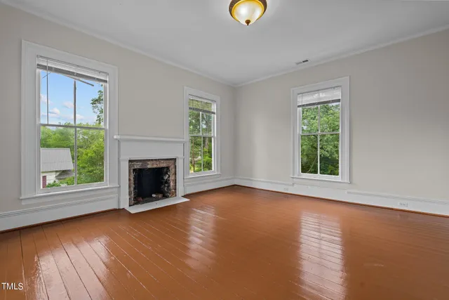 a view of an empty room with wooden floor windows and a fireplace