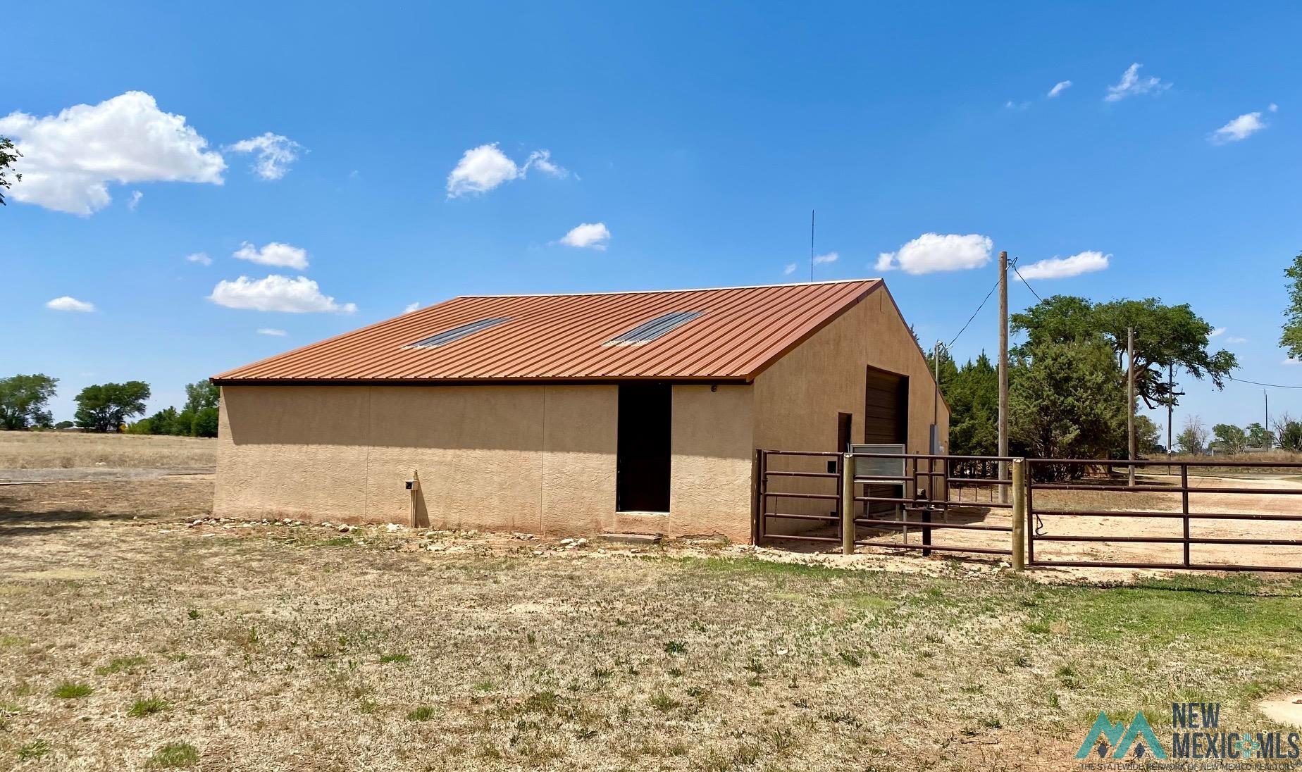 1131 Curry Road North Clovis, NM 88101 - Photo 62 of 69 Stucco-sided outbuilding with a terracotta-toned metal roof featuring multiple skylights