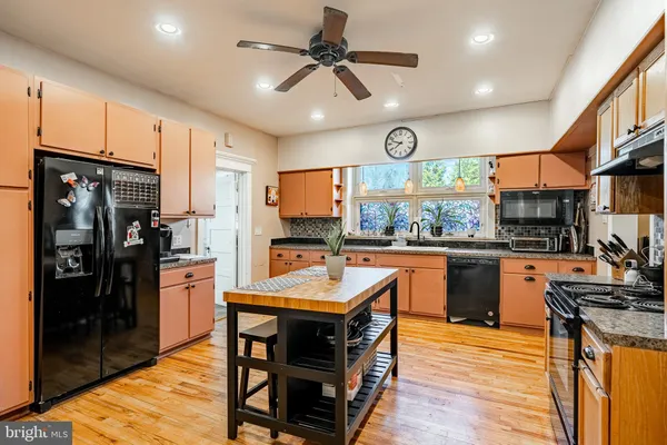 a kitchen with stainless steel appliances granite countertop a refrigerator a sink dishwasher a stove and white countertops with wooden floor