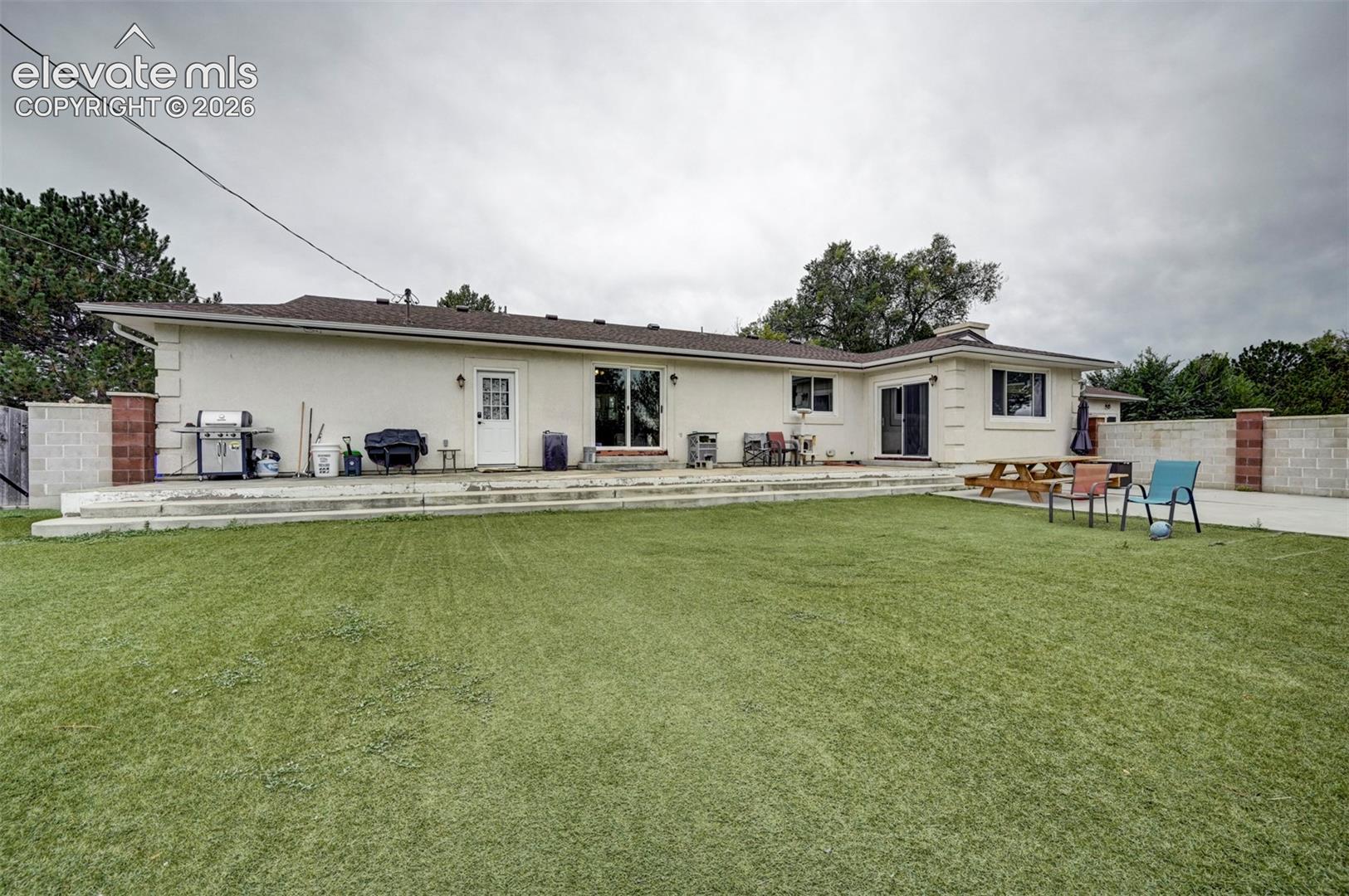 8170 Valli Farm Road Fountain, CO 80817 - Photo 42 of 50 Expansive artificial turf lawn with a multi-level concrete patio, stucco exterior, and sliding glass doors