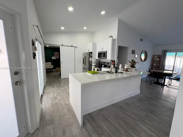 a large white kitchen with kitchen island a sink a stove a refrigerator and a dining table with wooden floor