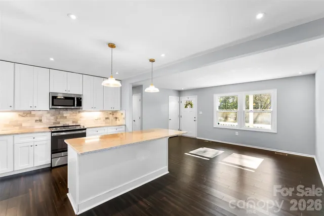 a large kitchen with stainless steel appliances granite countertop a stove a sink dishwasher a refrigerator white cabinets and wooden floor next to a window