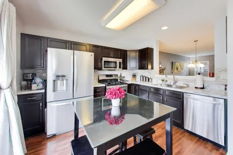 a kitchen with stainless steel appliances granite countertop a dining table chairs refrigerator and sink