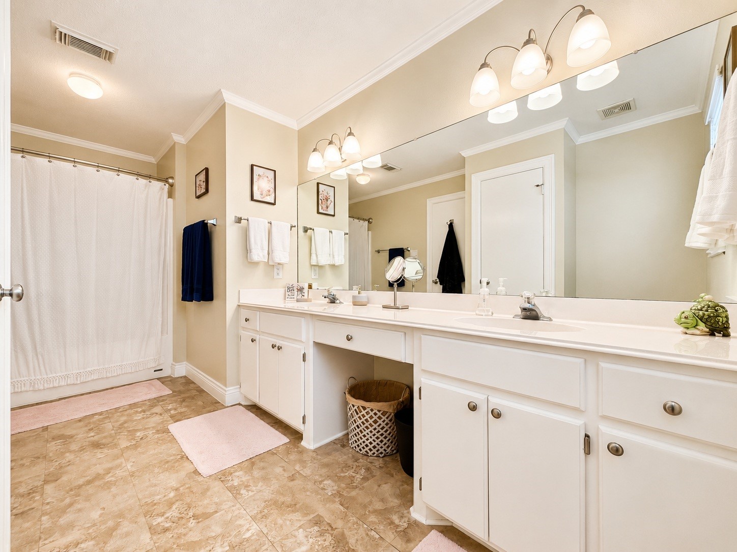 135 Sand Shoals Road Freeport, TX 77541 - Photo 13 of 20 This bathroom features a spacious double vanity with ample storage, a large mirror, and elegant lighting. The neutral color palette enhances the room's brightness, complemented by a tiled floor and a shower with a curtain.