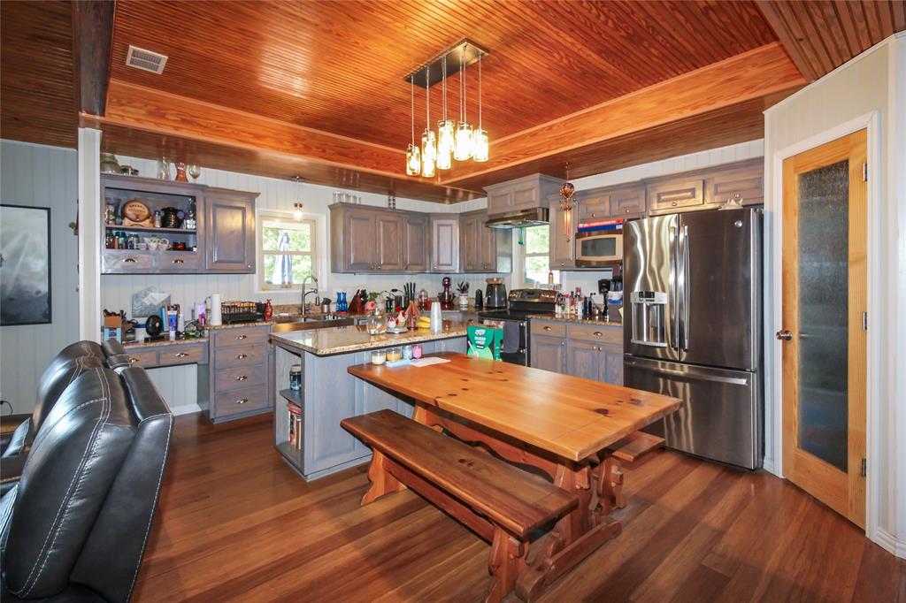 1001 Sandy Ridge Road Scurry, TX 75158 - Photo 15 of 35 Kitchen featuring wood-finish flooring, exposed wood beam ceiling, stainless steel appliances, grey cabinetry, and a central island with a stone countertop