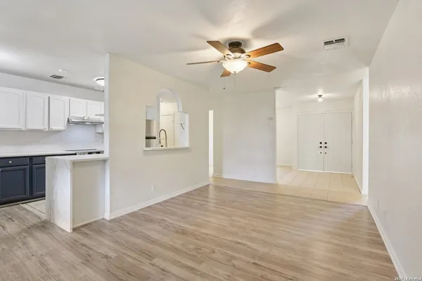a view of an empty room and kitchen with wooden floor