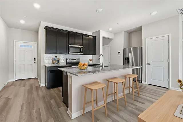 a kitchen with stainless steel appliances a stove top oven a refrigerator a sink and a dining table with wooden floor