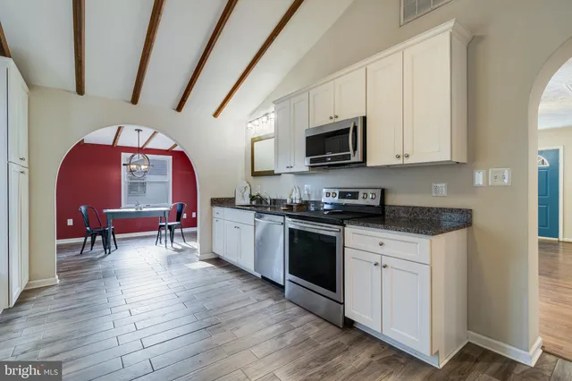 a kitchen with stainless steel appliances granite countertop a stove top oven a sink dishwasher and white cabinets with wooden floor