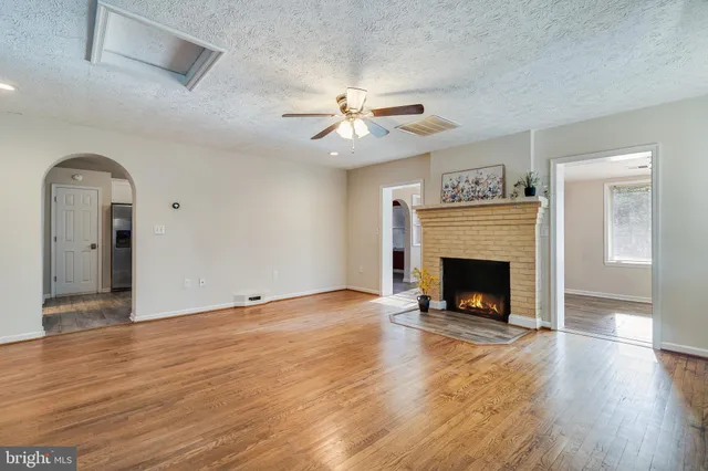 a view of an empty room with wooden floor a fireplace and a window