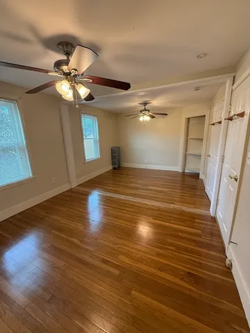 a view of an empty room with wooden floor and a ceiling fan
