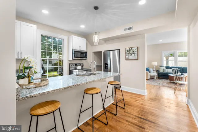 a kitchen with stainless steel appliances granite countertop a refrigerator a stove a sink a dining table and chairs with wooden floor