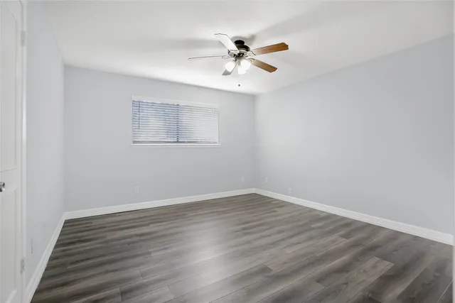 a view of an empty room with wooden floor and a ceiling fan