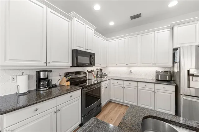 a kitchen with stainless steel appliances granite countertop a sink a stove a refrigerator and white cabinets with wooden floor