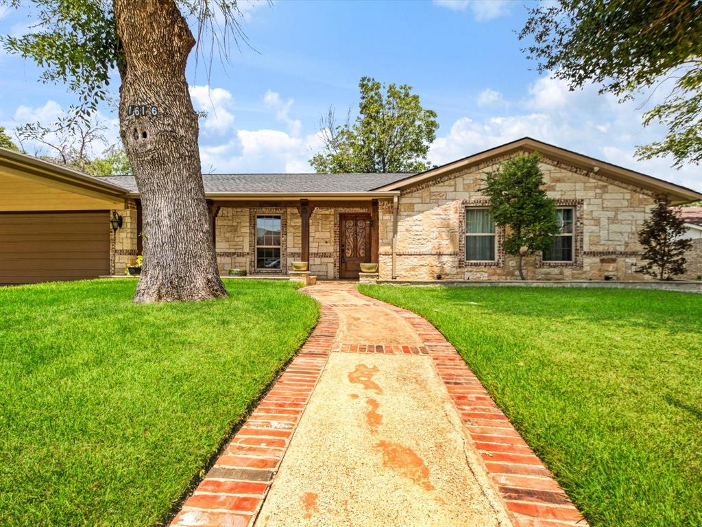 Stone exterior with a prominent mature tree, brick-edged pathway, covered entry, and attached garage