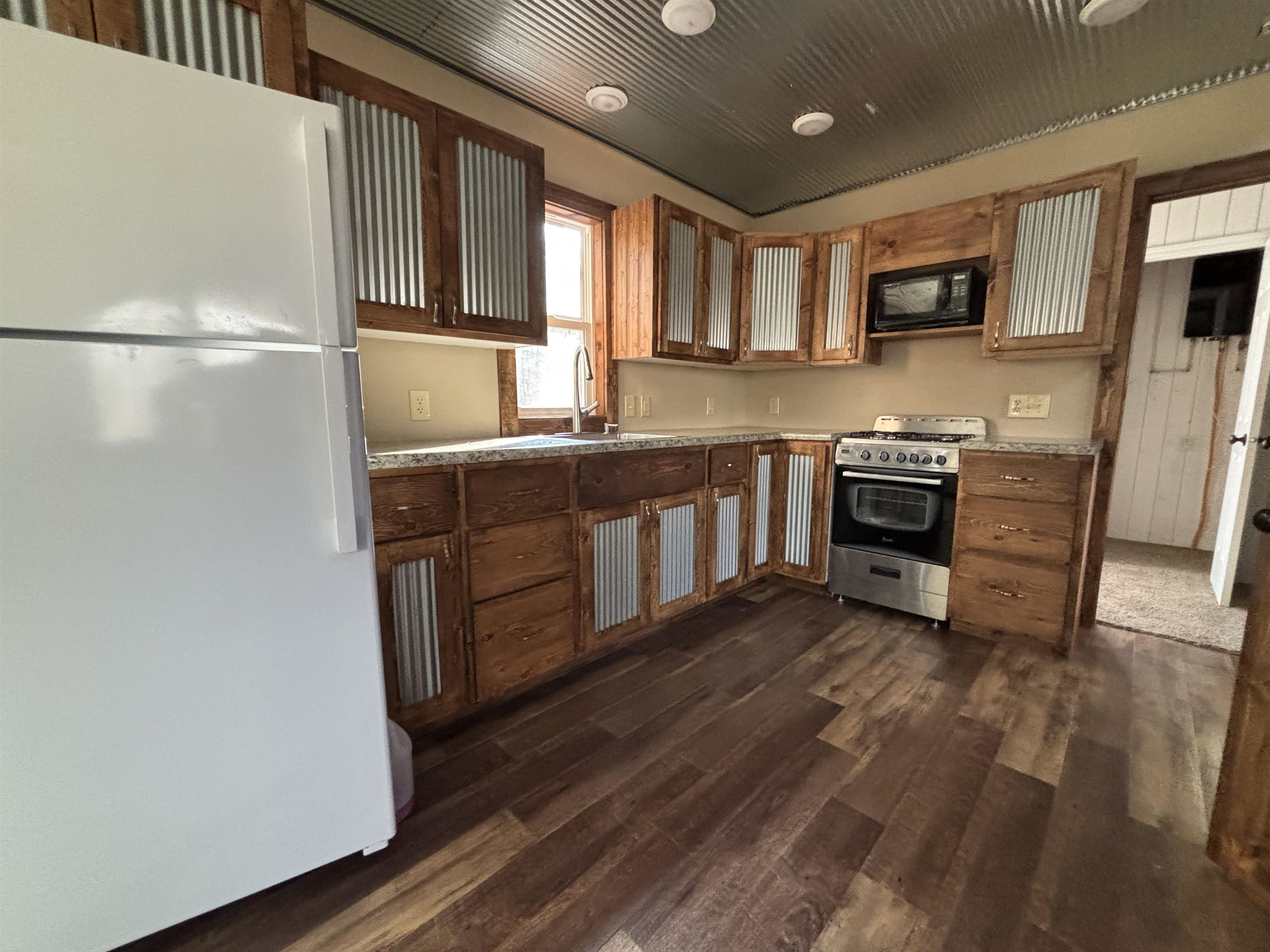 3746 South Hughes Road Hibbing, MN 55746 - Photo 5 of 10 Kitchen featuring freestanding refrigerator, gas range, brown cabinetry, black microwave, and light countertops