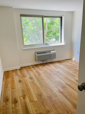 a view of an empty room with a window and wooden floor