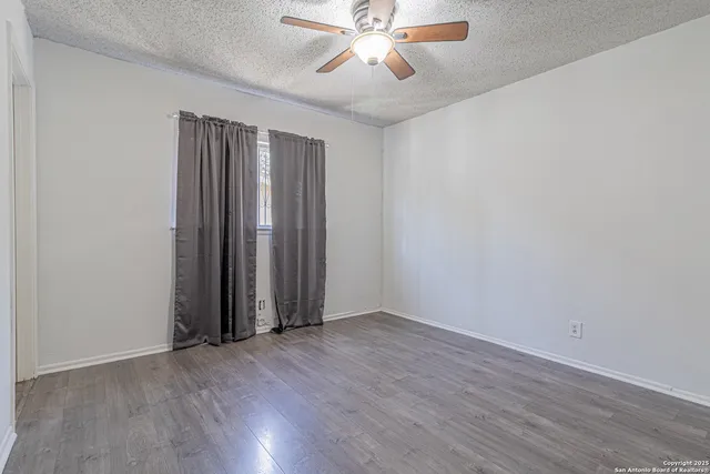 an empty room with wooden floor fan and windows