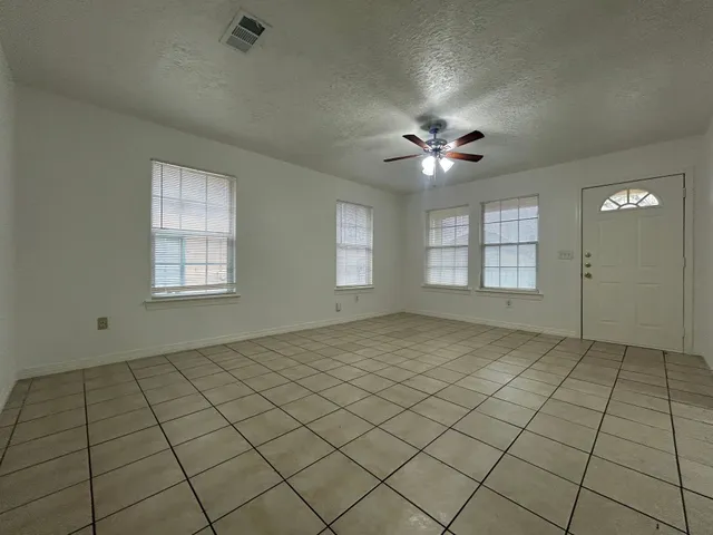 an empty room with chandelier fan and windows