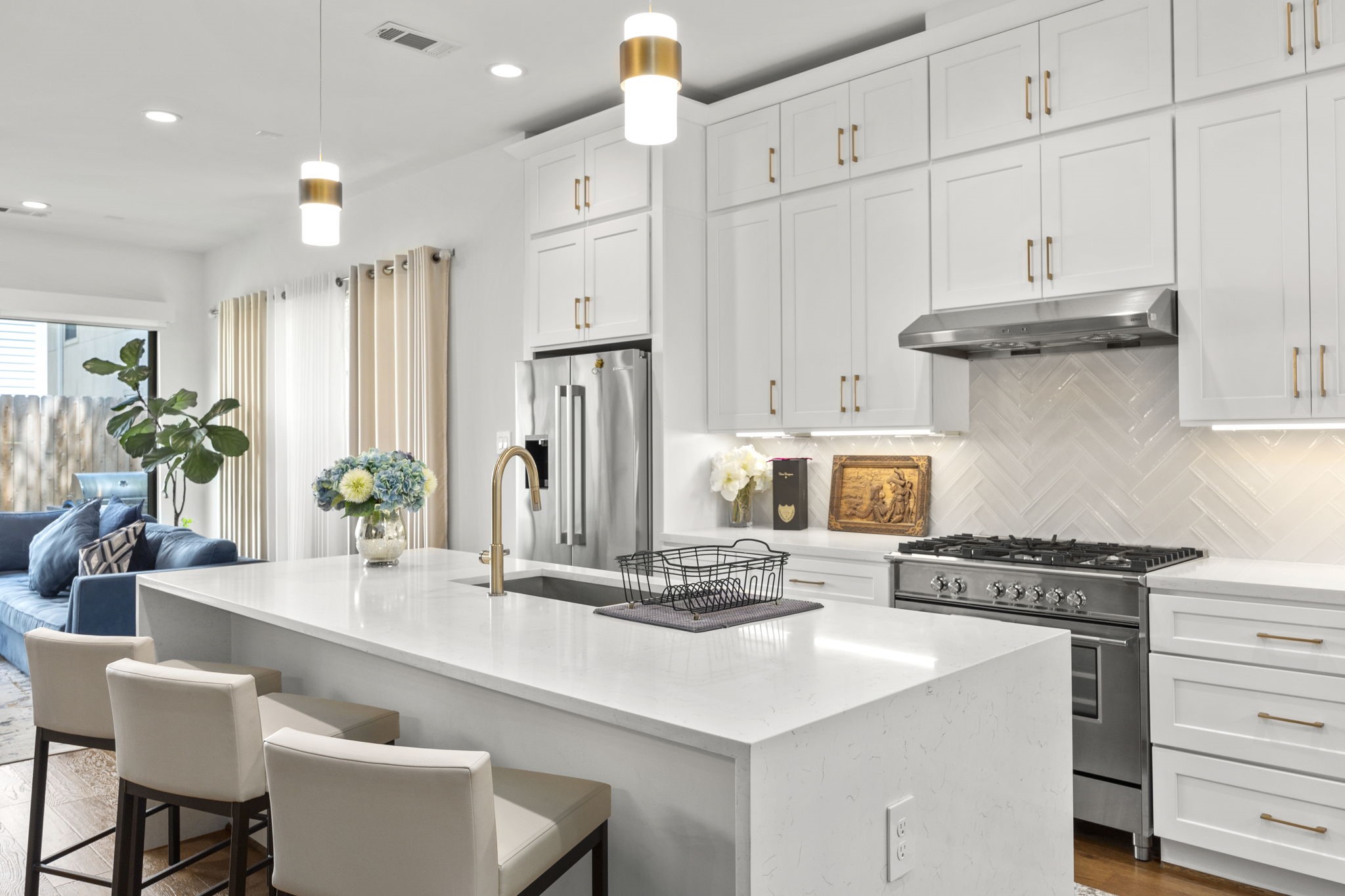 2411 Hazard Street Houston, TX 77019 - Photo 12 of 46 This gourmet kitchen is a chef's dream, featuring sleek stainless steel appliances, a large gas range, and a stylish herringbone tile backsplash. The expansive quartz island offers plenty of prep space, complemented by elegant gold fixtures and custom cabinetry for a clean, modern aesthetic.