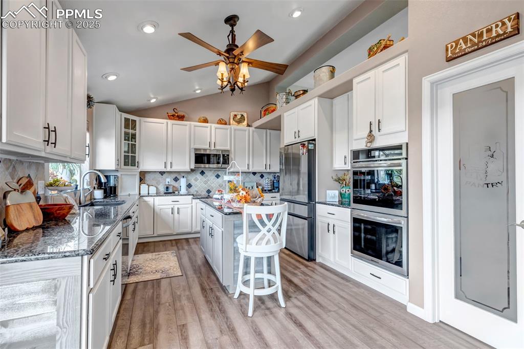7120 Highcroft Drive Colorado Springs, CO 80922 - Photo 13 of 50 a kitchen with stainless steel appliances a refrigerator a stove top oven a sink dishwasher and white cabinets with wooden floor