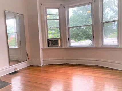 an empty room with wooden floor cabinet and windows