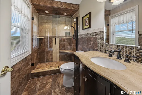 a bathroom with a granite countertop sink a toilet a mirror and shower
