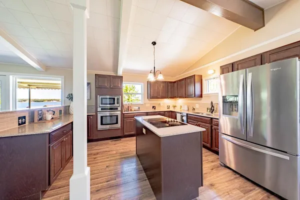 a kitchen with stainless steel appliances granite countertop a refrigerator a sink dishwasher a oven and a dining table with wooden floor