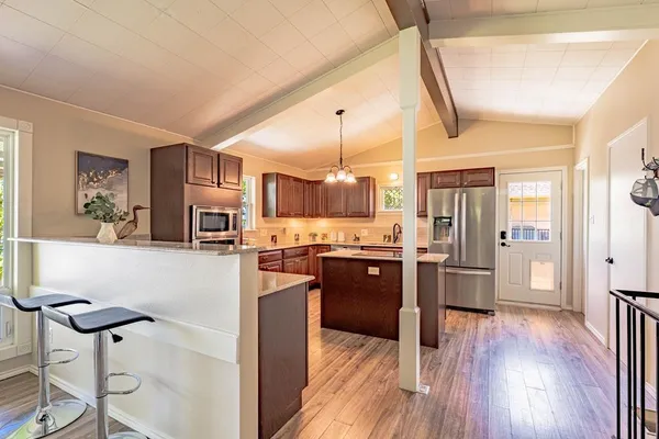 a kitchen with stainless steel appliances kitchen island granite countertop a refrigerator a stove and white cabinets with wooden floor