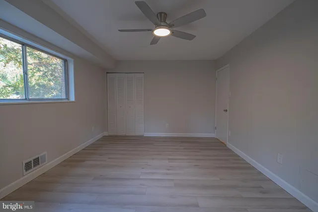 an empty room with wooden floor ceiling fan and windows