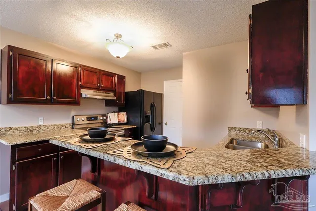 a kitchen with stainless steel appliances granite countertop a sink dishwasher stove and refrigerator with wooden cabinets