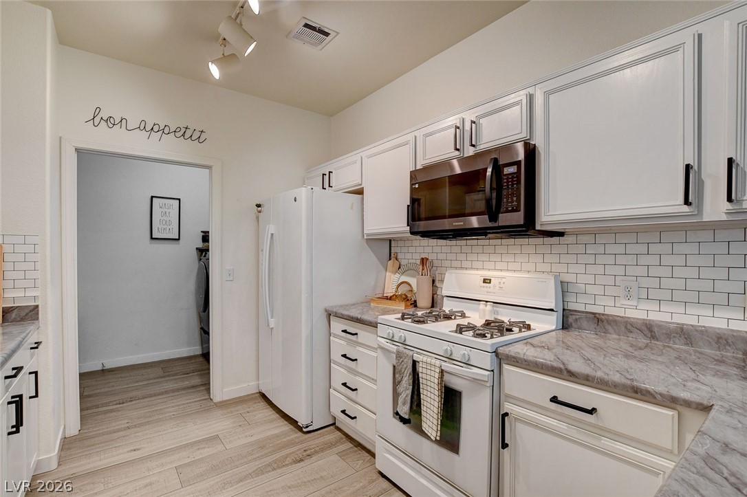 64 Brown Swallow Way Henderson, NV 89012 - Photo 15 of 42 Kitchen featuring white appliances, tasteful backsplash, light countertops, light wood-style floors, and white cabinetry