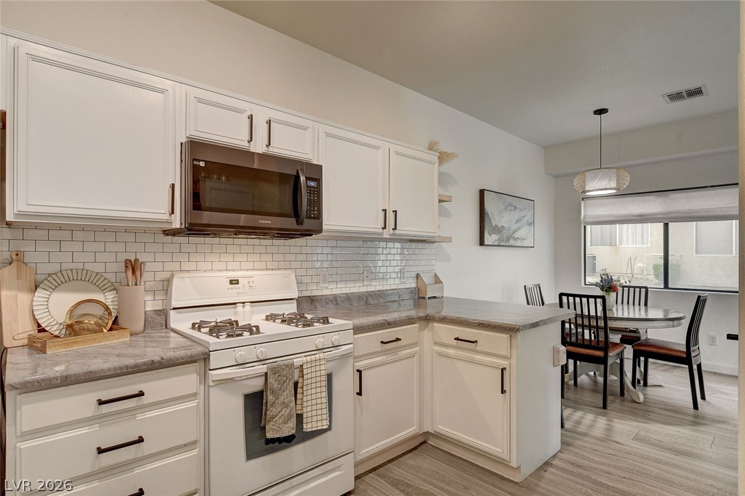 64 Brown Swallow Way Henderson, NV 89012 - Photo 17 of 42 Kitchen featuring gas range gas stove, a peninsula, stainless steel microwave, hanging light fixtures, and light countertops