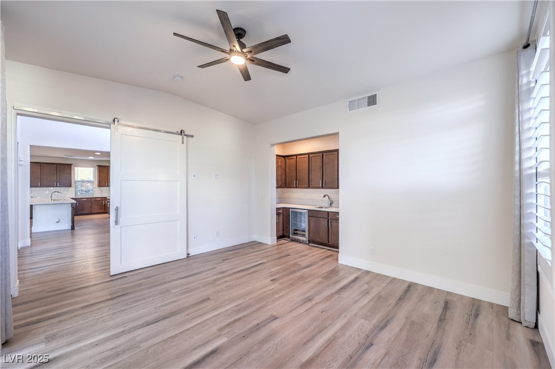 9655 Skye Star Avenue Las Vegas, NV 89166 - Photo 15 of 46 Unfurnished living room with a barn door, light wood-style flooring, wine cooler, vaulted ceiling, and a ceiling fan