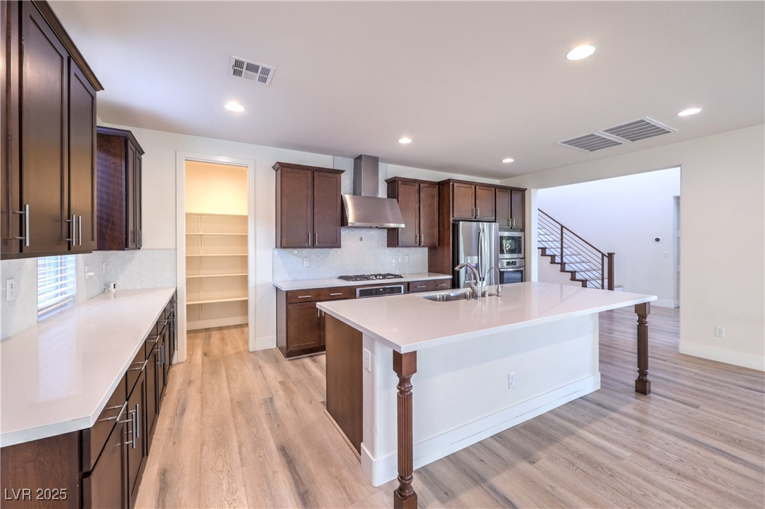 9655 Skye Star Avenue Las Vegas, NV 89166 - Photo 35 of 46 Kitchen with decorative backsplash, dark brown cabinetry, an island with sink, stainless steel appliances, and wall chimney range hood