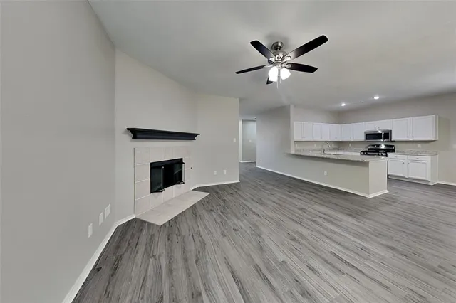 a view of a livingroom with a fireplace a ceiling fan and wooden floor