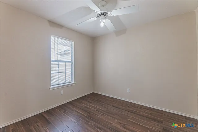 an empty room with wooden floor chandelier fan and windows
