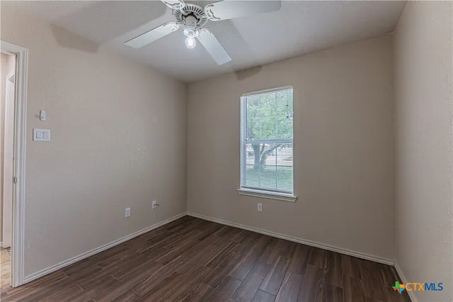 an empty room with wooden floor fan and windows