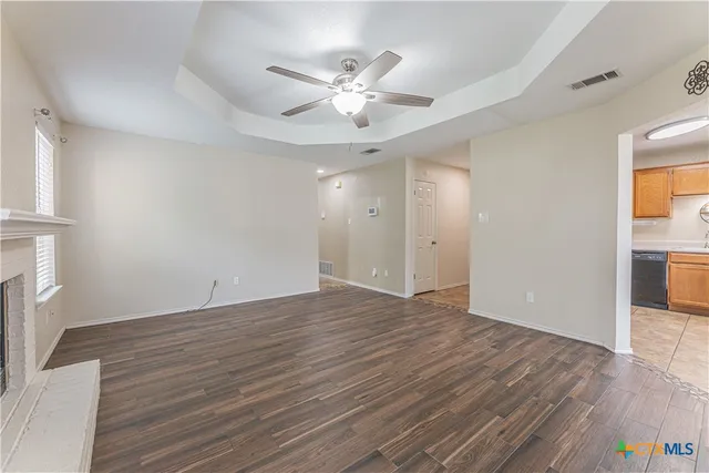 a view of an empty room with wooden floor and a ceiling fan