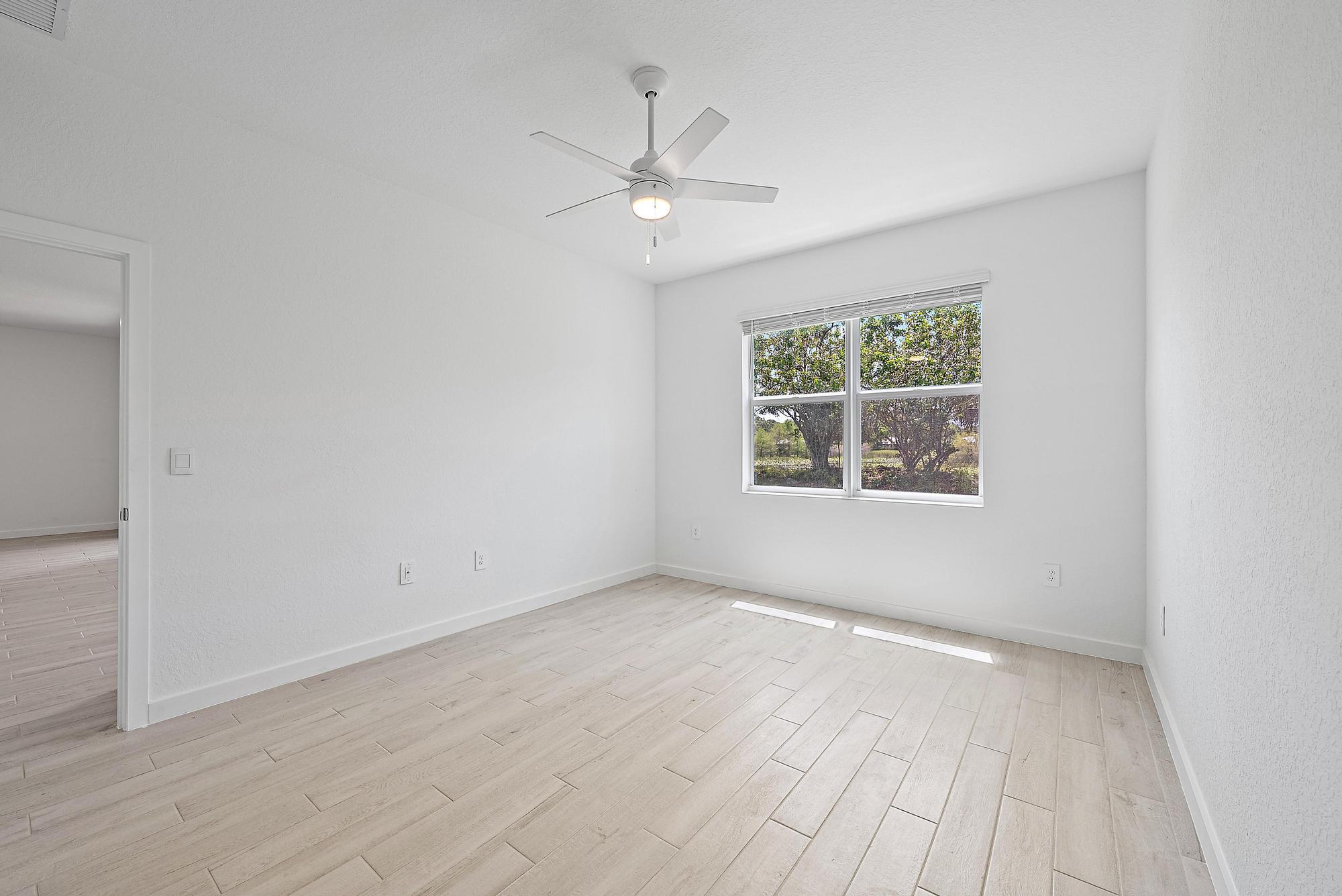 5880 Southeast Sky Blue Circle Stuart, FL 34997 - Photo 16 of 48 an empty room with wooden floor chandelier fan and windows