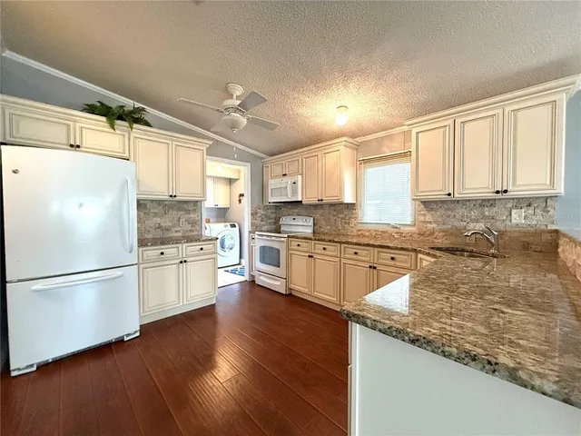 a kitchen with stainless steel appliances granite countertop a refrigerator a sink dishwasher a stove and white countertops with wooden floor