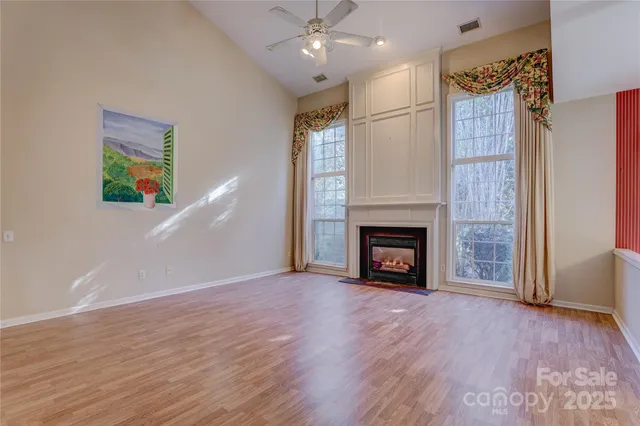 a view of an empty room with wooden floor fireplace and a window