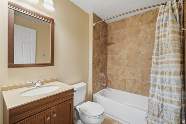 5576 South 4100th Street West Roy, UT 84067 - Photo 30 of 35 Bathroom featuring a vanity with a light-toned countertop, a wood-framed mirror, a toilet, a bathtub with a shower, and tiled shower walls
