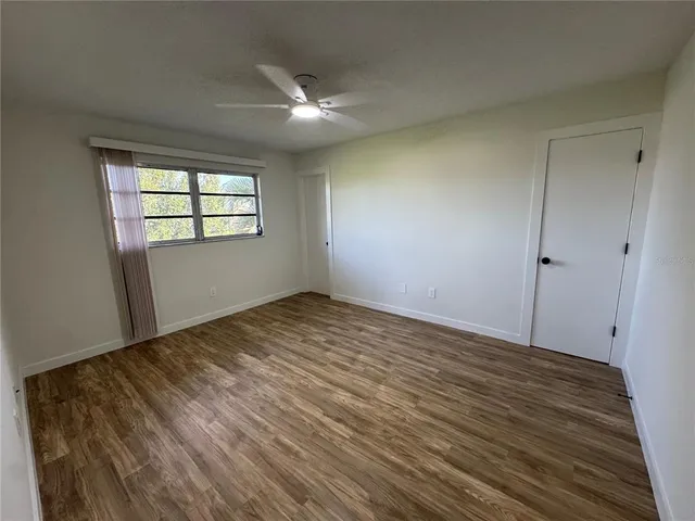 a view of empty room with wooden floor and fan