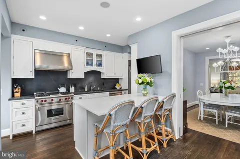 a kitchen with stainless steel appliances granite countertop a stove top oven a sink a dining table and chairs with wooden floor