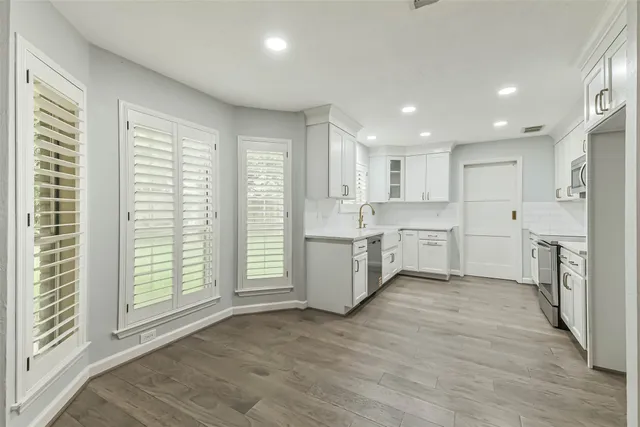 a large kitchen with a large counter top a sink stainless steel appliances and cabinets