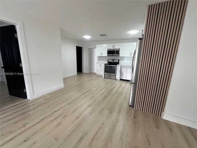 an empty room with wooden floor kitchen view and a refrigerator
