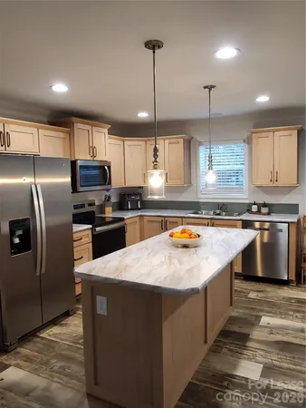 a kitchen with stainless steel appliances granite countertop a refrigerator a sink dishwasher a stove and white cabinets with wooden floor
