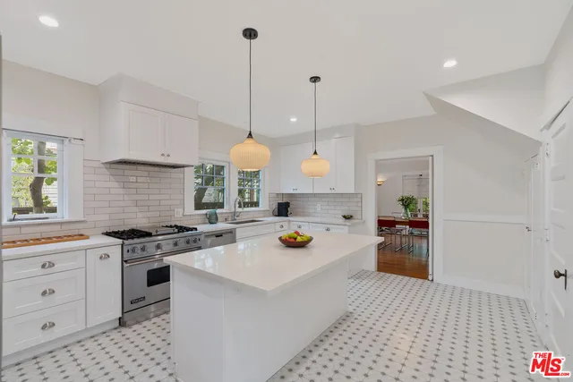 a kitchen with stainless steel appliances a stove a sink a chimney a refrigerator and cabinets